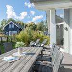Terrasse mit Tisch und Stühlen. Im Hintergrund ein blaues Haus und Grünflächen.