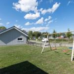 Ein graues Ferienhaus mit Garten, Spielplatz und Terrasse unter blauem Himmel.