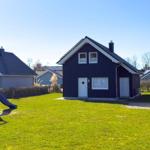 Schwarzes Holzhaus mit weißem Fensterrahmen und Spielplatz im Vorgarten.