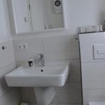 Badezimmer mit Waschbecken, Spiegel, Toilette und Stehleuchte.