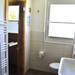 Badezimmer mit Toilette, Waschbecken und Dusche. Fenster sorgt für Tageslicht.