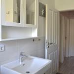 Badezimmer mit Waschbecken, Spiegelschrank und offener Tür zum Flur.