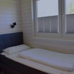 Ein Bett mit weißer Bettwäsche und dunklem Kopfteil neben einem Fenster mit Jalousien.