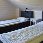 Zwei Einzelbetten mit weißen Bettwäsche und grauen Kopfenden in einem schrägen Dachzimmer mit Holzwand.