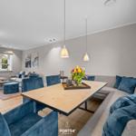 Essbereich mit Holztisch, blauen Stühlen und Sofa. Kamin und Fenster sichtbar.