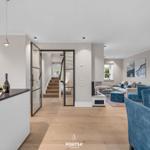 Offener Wohnbereich mit Essbereich, Küche und Treppenaufgang. Blaue Sessel und Kamin.