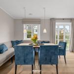 Essbereich mit Tisch, blauen Stühlen und Sofa. Fenster und Glastür zeigen Garten.