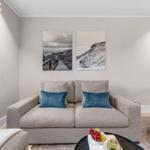 Ein Wohnzimmer mit grauem Sofa, zwei blauen Kissen und zwei Wandbildern über dem Sofa.