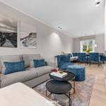 Wohn- und Essbereich mit Kamin, Sofa und blauen Sesseln.