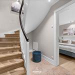 Treppenhaus mit Holztreppe und Blick in Schlafzimmer mit Bett und Wandbildern.