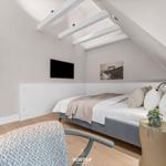 Schlafzimmer mit Dachschrägen, Bett, Fernseher und Pflanze.