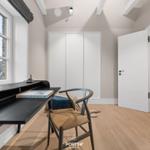 Schlafzimmer mit Schreibtisch, Stuhl und Kleiderschrank. Holzboden und großes Fenster.