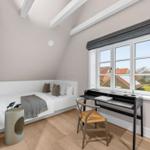 Schlafzimmer mit Dachschrägen, Bett, Schreibtisch und Fenster mit Blick.