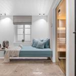 Ein Raum mit Bett, Fenster und Sauna. Wandbilder und Bodenfliesen sind sichtbar.