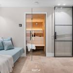 Sauna mit Holzbank und Glaswand. Sofa mit Kissen und Decke.