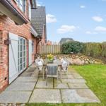 Roter Backsteinbau mit Terrasse und Garten. Holztisch mit Stühlen und Blumen.