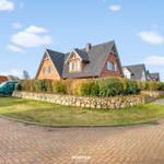 Rotes Backsteingebäude mit Steinmauer und Rasenfläche. Parkplatz mit grüner Van.