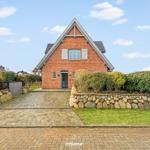 Rotes Backsteingebäude mit Steinmauer und Kiesweg. Eingangstür offen. Hinterhof mit Grünflächen.