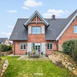 Rotes Backsteingebäude mit Garten und Terrasse. Holztisch und Stühle stehen draußen.