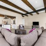 Wohnbereich mit Sofa, TV und Küchenbereich. Holzbalken an der Decke.