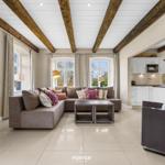 Wohnzimmer mit Ecksofa, Holzbalken und Küchenbereich im Hintergrund.