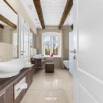 Badezimmer mit Waschbecken, Fenster und Toilette. Holzbalken an der Decke.