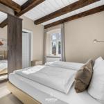 Schlafzimmer mit Doppelbett, Holzbalken und Fenster. Spiegel reflektiert ein weiteres Bett.