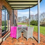 Terrasse mit Sitzgruppe, pinkem Handtuch und Blick auf grünen Garten.