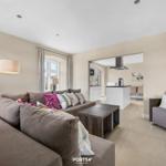 Wohnzimmer mit Sofa, Sessel und Küchenbereich im Hintergrund.