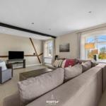 Wohnzimmer mit Sofa, Sessel, Fernseher und großen Fenstern.