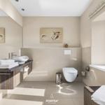 Badezimmer mit Waschtisch, Toilette und Fenster. Wandbilder und Handtuchstapel sichtbar.