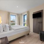 Schlafzimmer mit Doppelbett, TV und Fenstern zum Garten.