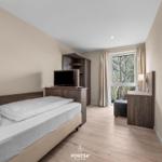 Schlafzimmer mit Bett, TV und Fensterblick auf Bäume.