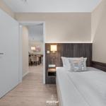 Schlafzimmer mit Bett und Holzpaneelen. Durchgang zum Essbereich mit Tisch und Stühlen.