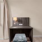 Schreibtisch mit Sitzbank, Wandlampe und Spiegel neben Fenster mit Blick auf Grünfläche.