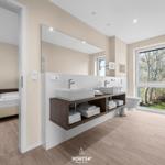 Badezimmer mit Doppelwaschbecken und Blick auf Garten. Schlafzimmer im Hintergrund.