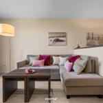 Wohnzimmer mit Ecksofa, Tisch und Wandbildern.