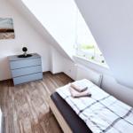 Schlafzimmer mit Dachschrägen, Bett, Kleiderschrank und Fenster.