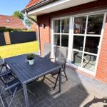 Terrasse mit Tisch, Stühlen und Sonnenschutz. Hintergrund: Garten und Hauswand.