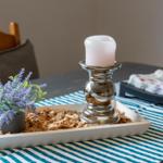 Tisch mit Kerze, Pflanze und Holzmulch auf Streifen-Tischdecke