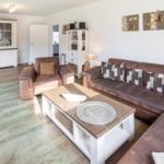 Wohnzimmer mit braunem Sofa, Holzfußboden und weißen Schränken.