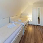 Zimmer mit zwei Einzelbetten, Holzboden und weißem Schrank