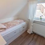 Schlafzimmer mit Dachschräge, Bett mit Schubladen, Fenster mit Vorhang und Heizkörper.