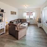 Wohnzimmer mit braunem Sofa, Holzboden und großen Fenstern.