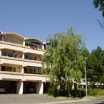 Multi-family building with balconies and parking spaces under trees.