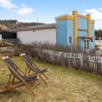 Two deck chairs sit on a lawn in front of a blue house with a white fence.