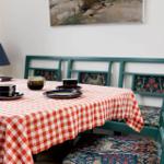 Dining table with checkered tablecloth and green chairs with floral upholstery.