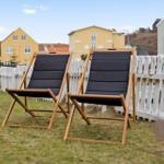Two black lounge chairs are on a lawn behind a white fence.