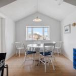 Dining room with round table, white chairs, and blue dresser. Wooden floor and window with view.