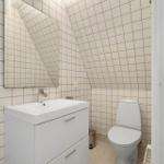 Bathroom with toilet, sink, and mirror on sloped walls.
